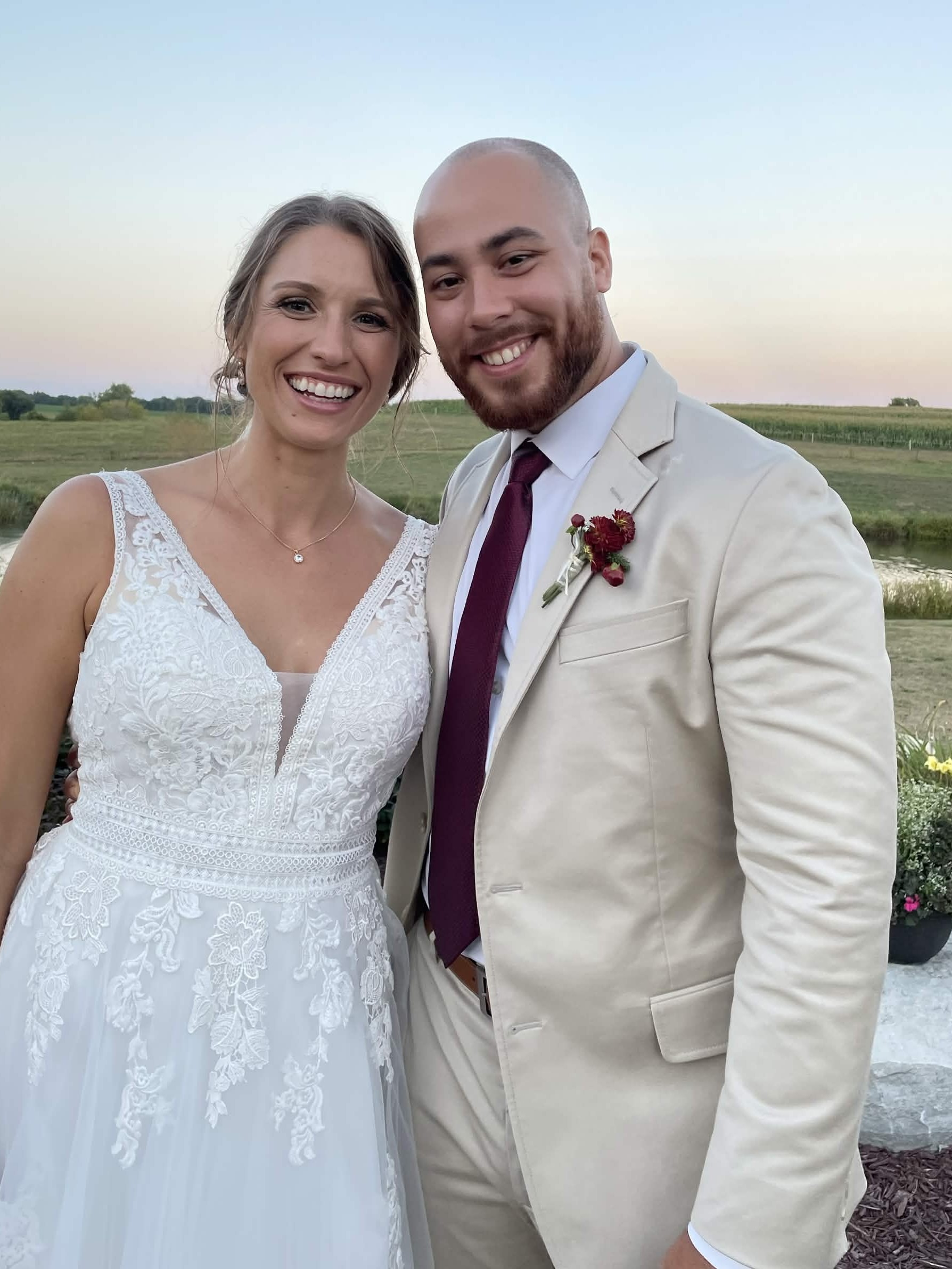 Couple at an outdoor wedding, groom in a fitted cream suit and bride in a white lace gown