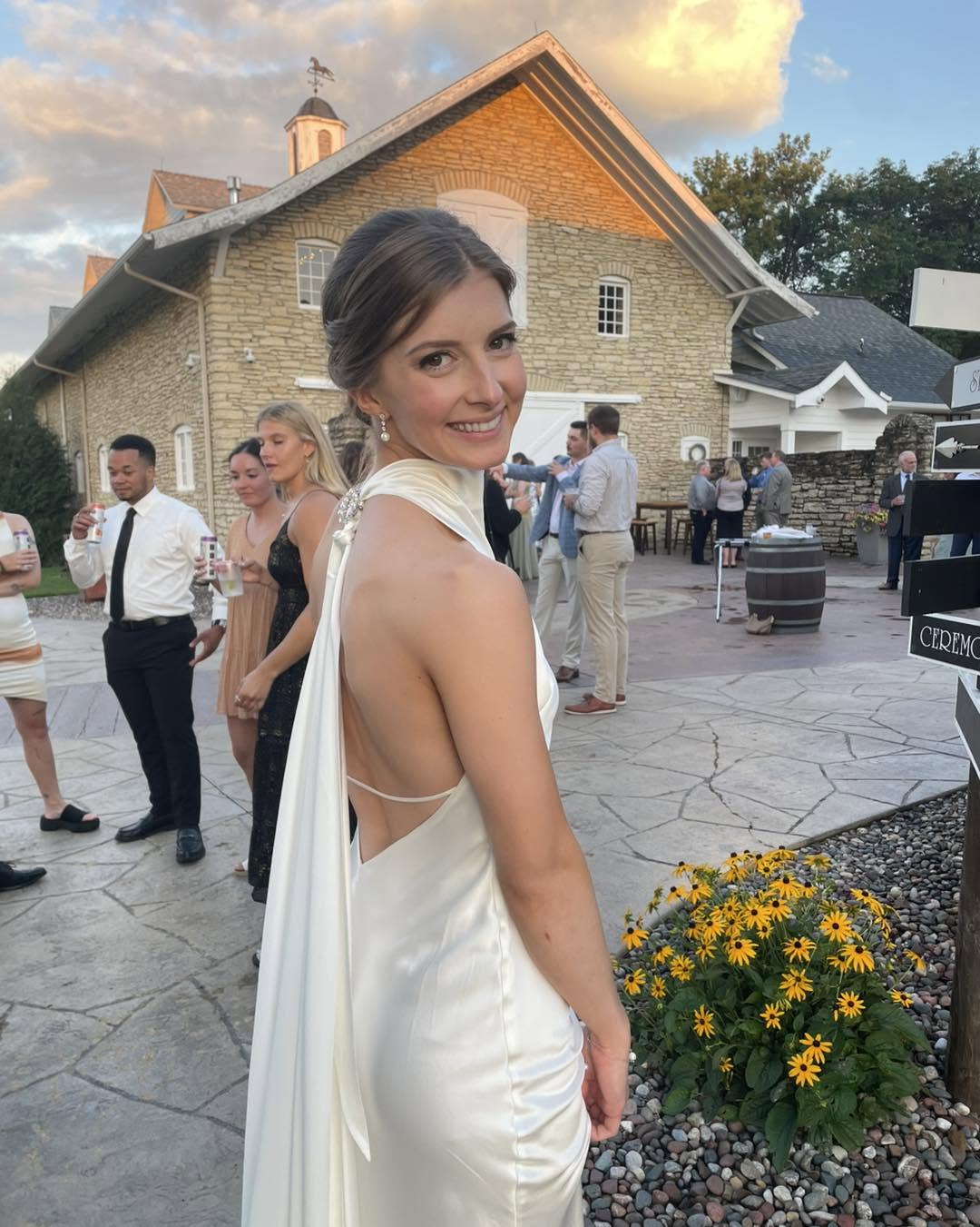 Bride in a fitted white halter gown holding a bouquet at a rustic stone venue
